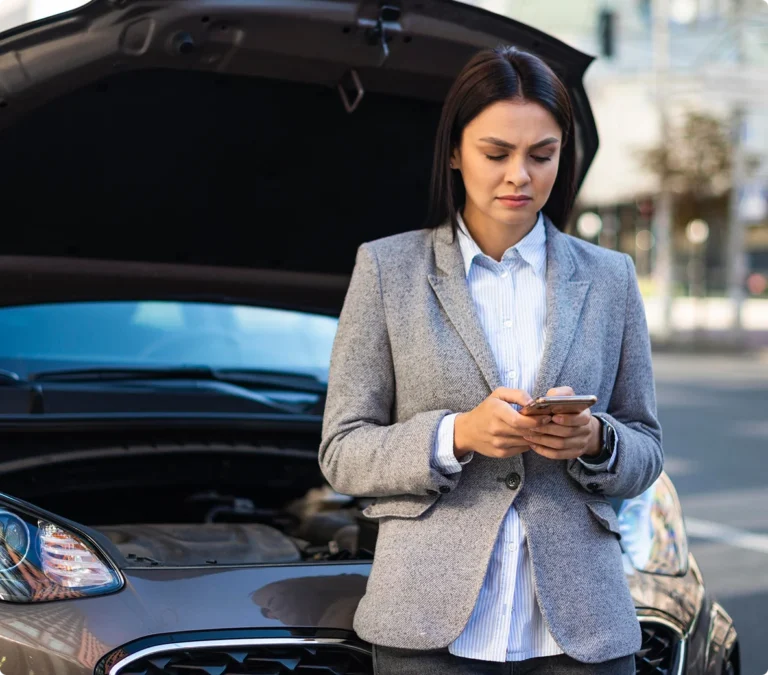 woman using her phone in front of her stalled car